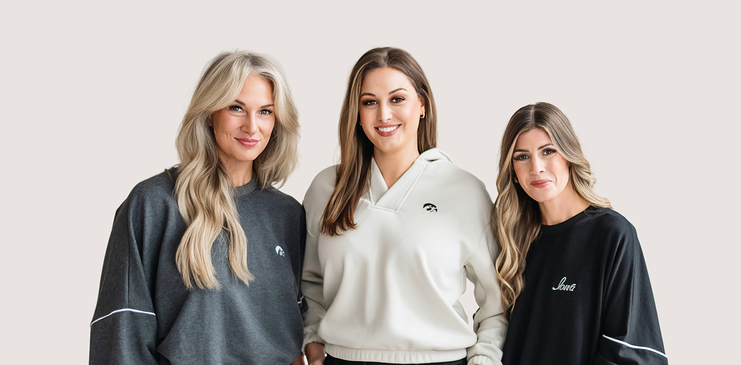Three women wearing stylish, high quality hoodies and crew neck sweatshirts with University of Iowa logos.
