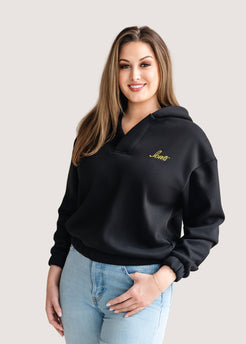Woman wearing a black hoodie with a gold Iowa script logo.