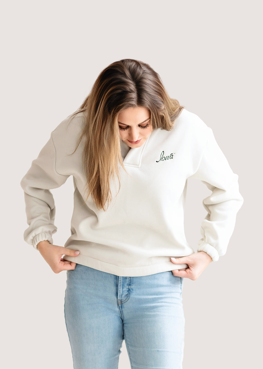 Woman wearing an ivory hoodie with a black Iowa script logo