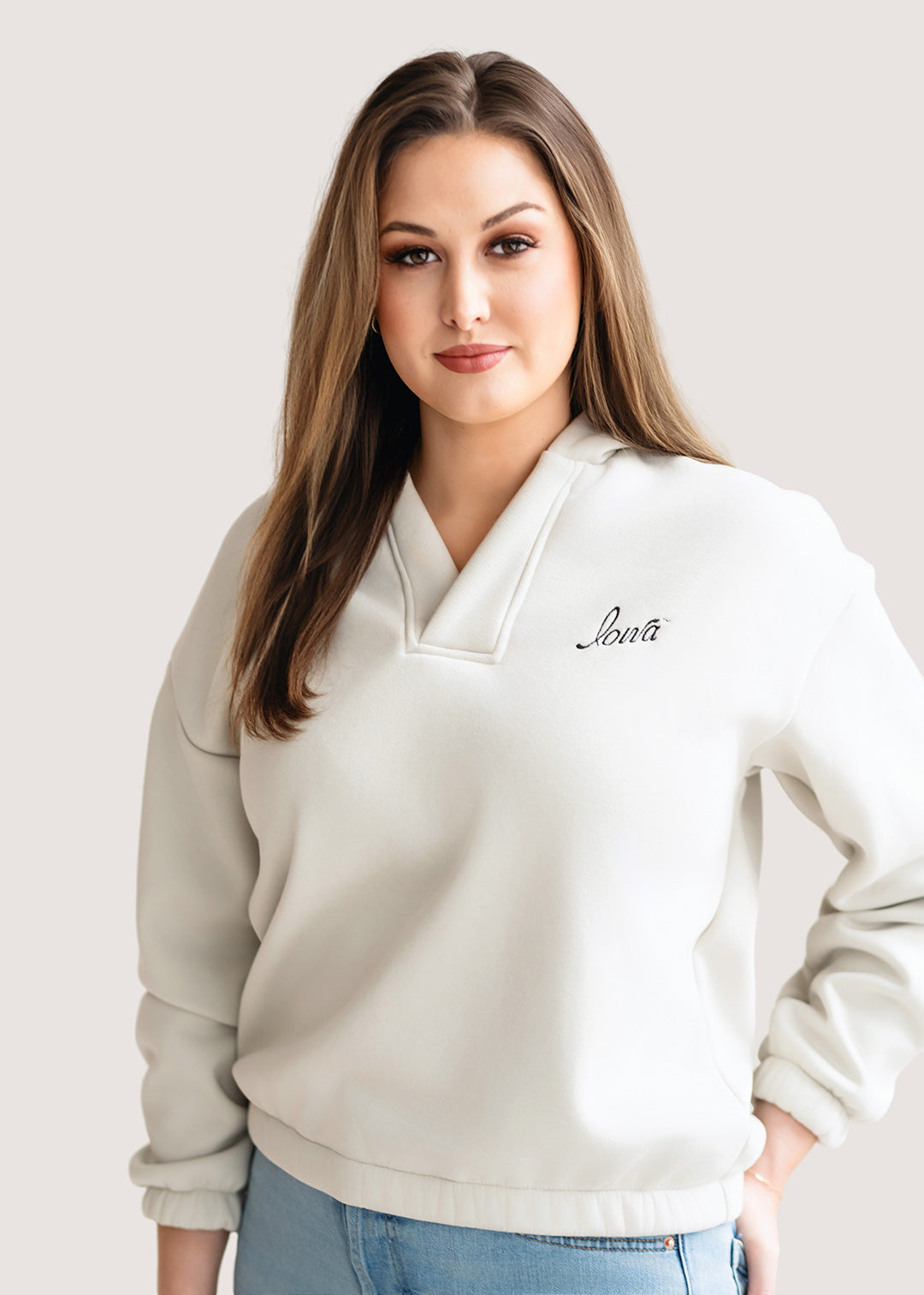 Woman wearing an ivory hoodie with a black Iowa script logo