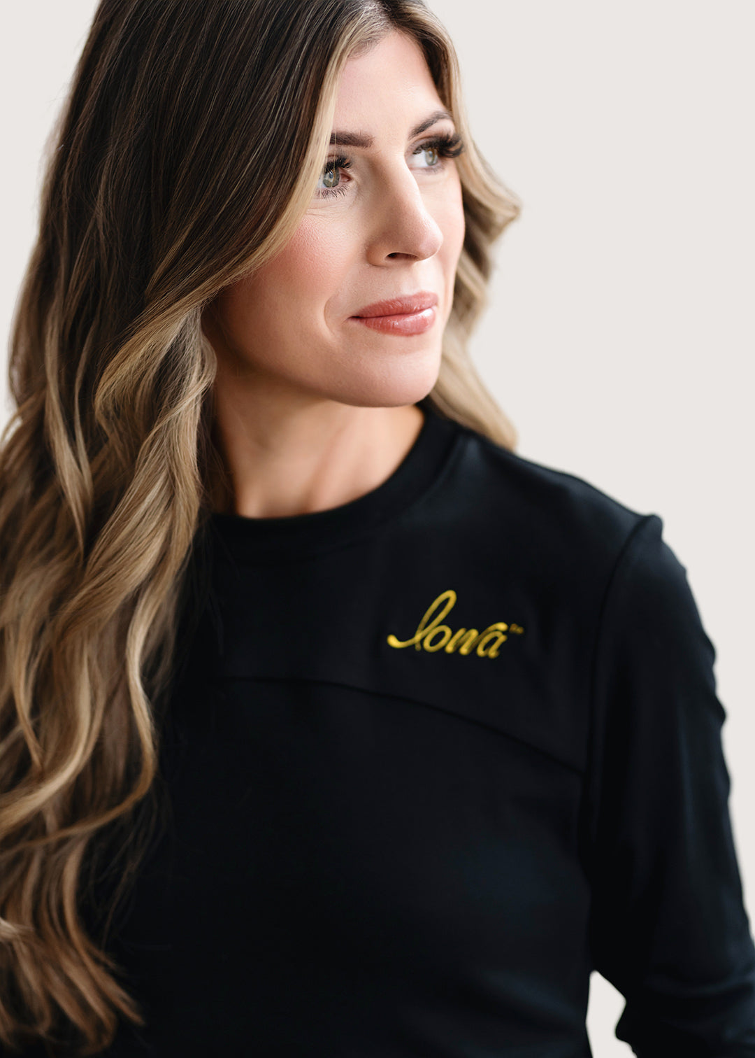 Woman wearing a long sleeve black shirt with a gold Iowa script logo.