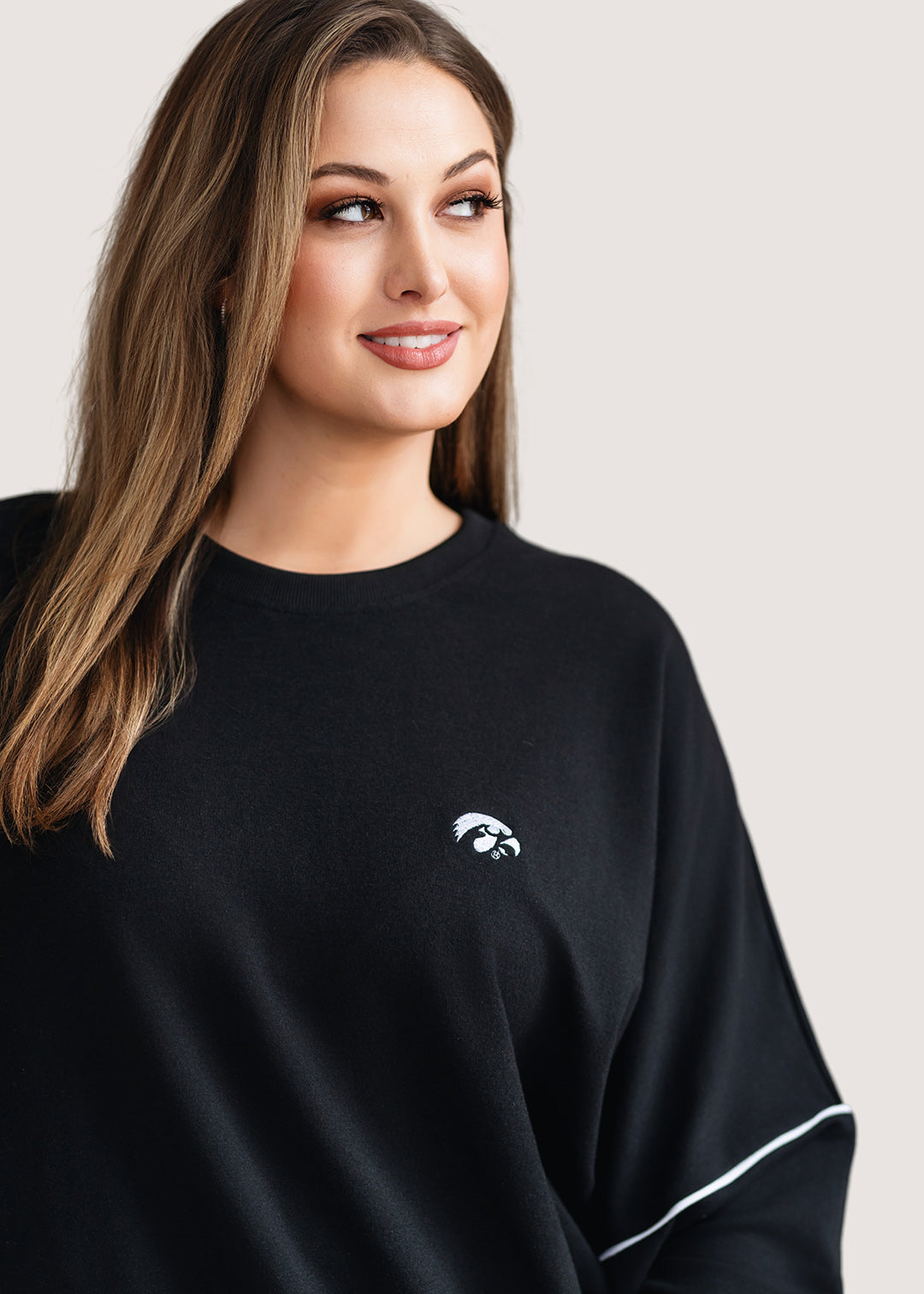 Woman wearing a black, drop shoulder sweatshirt with white trim and a white Tigerhawk logo.