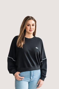 Woman wearing a black, drop shoulder sweatshirt with white trim and a white Tigerhawk logo.