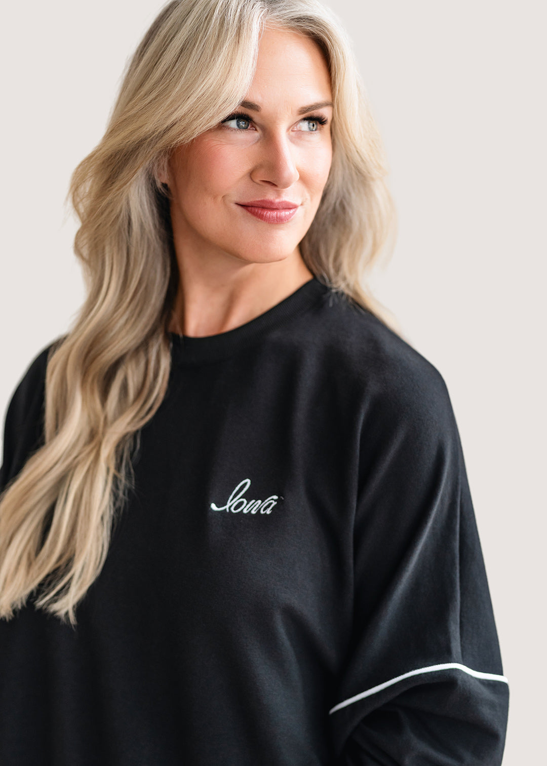 Woman wearing a black sweatshirt with 'Lover' embroidered on it against a plain background