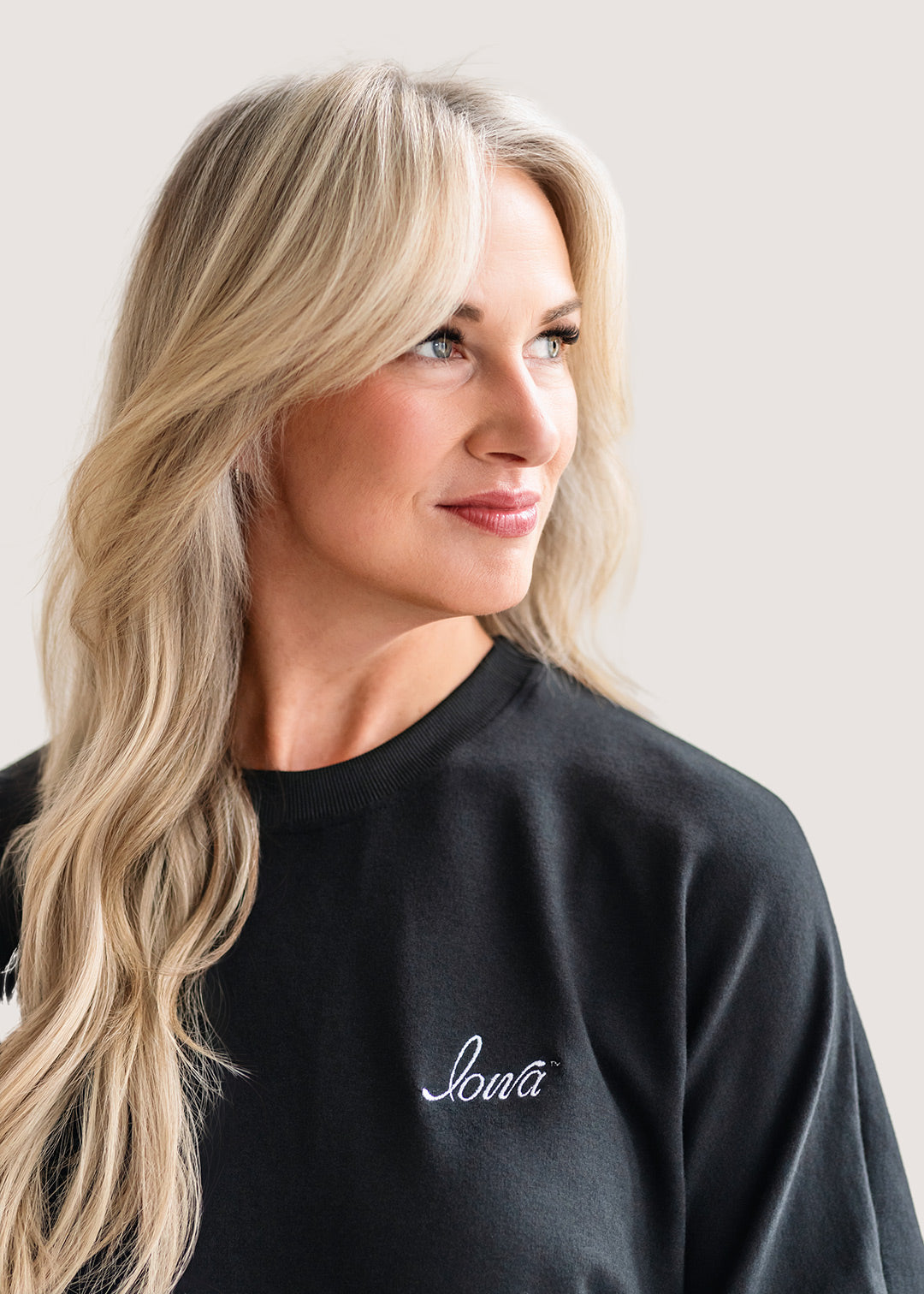 Woman wearing a black sweatshirt with 'Iowa' embroidered on it against a plain background.