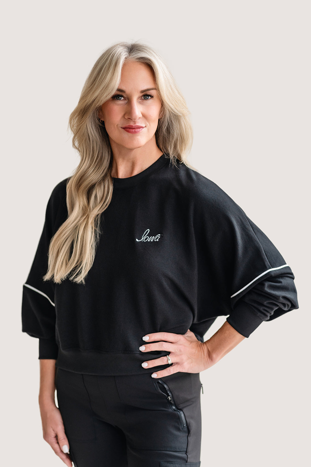 Woman wearing a black, drop shoulder sweatshirt with white trim and a white Iowa script logo.