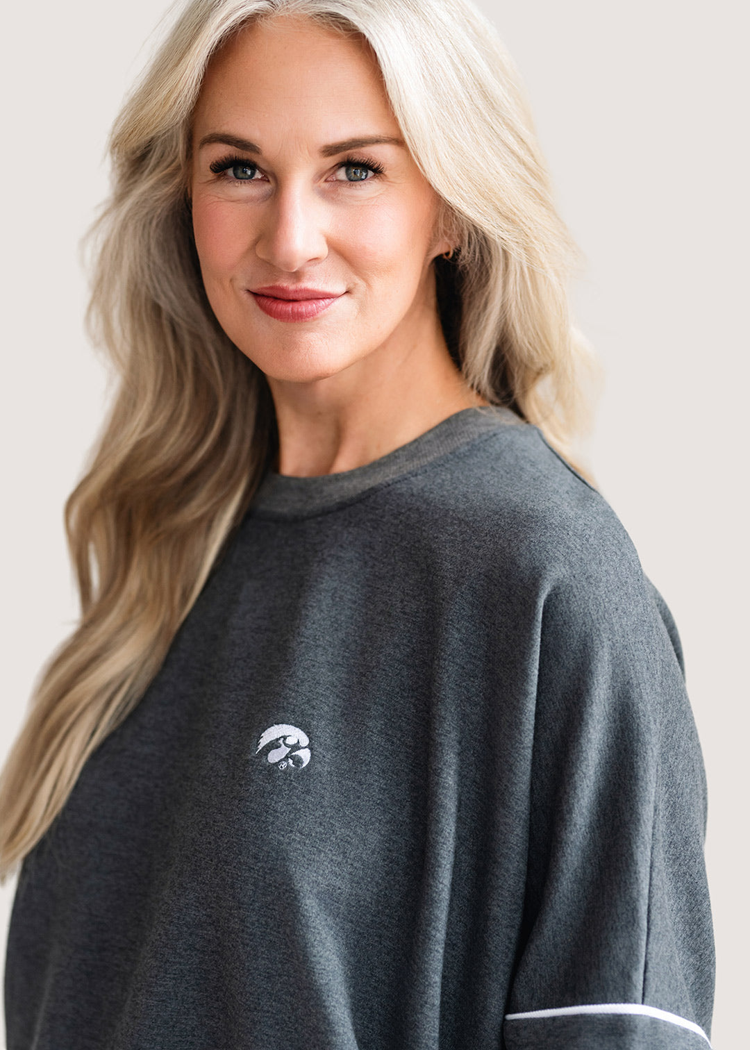 Woman wearing a grey, drop shoulder sweatshirt with white trim and a white Tigerhawk logo.