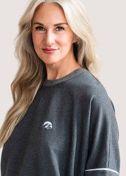 Woman wearing a grey, drop shoulder sweatshirt with white trim and a white Tigerhawk logo.