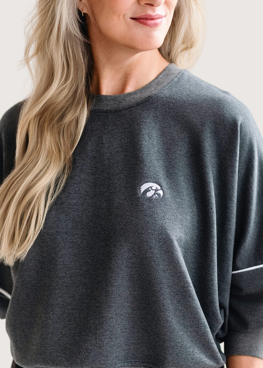 Woman wearing a grey, drop shoulder sweatshirt with white trim and a white Tigerhawk logo.