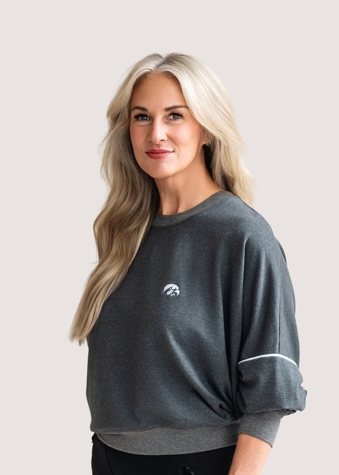 Woman wearing a grey, drop shoulder sweatshirt with white trim and a white Tigerhawk logo.