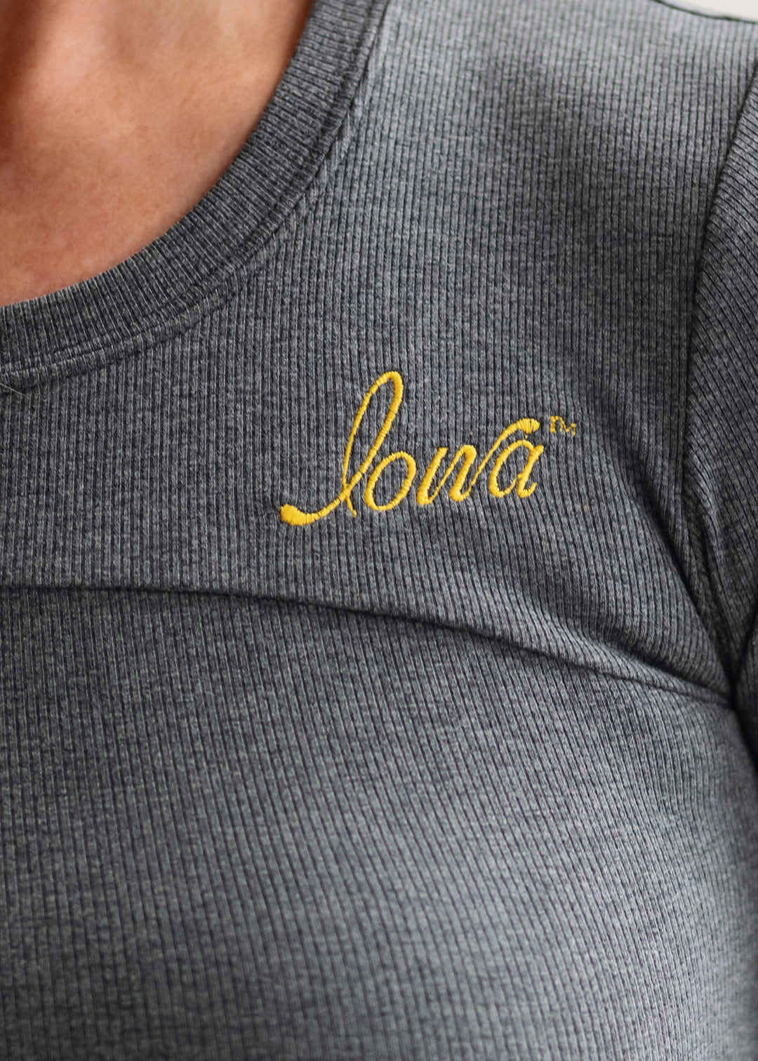 Woman wearing a grey ribbed long sleeve shirt with a gold Iowa script logo.