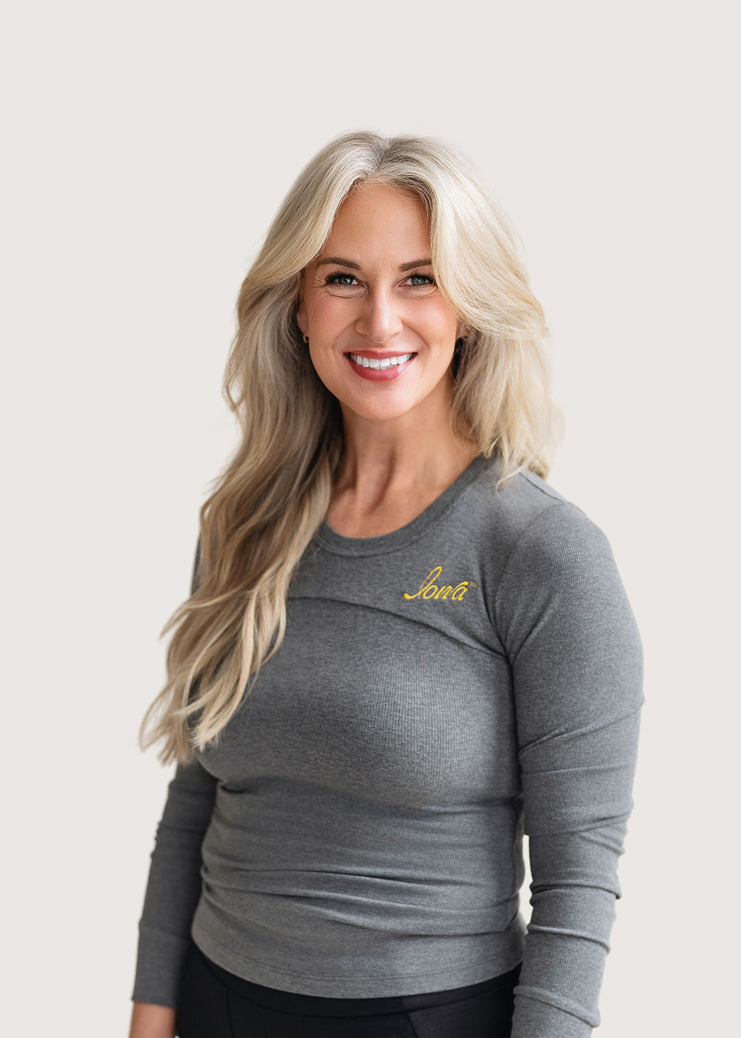 Woman wearing a grey ribbed long sleeve shirt with a gold Iowa script logo.